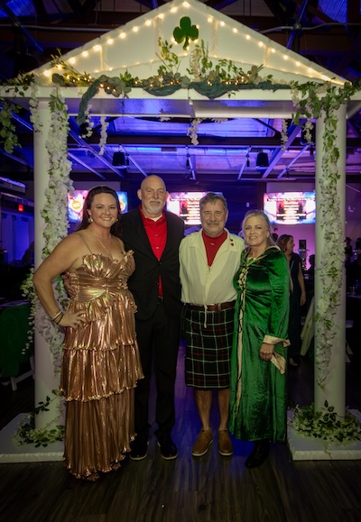 Members posing under the decorated arch at the Shamrock-n-Roll Mardi Gras Ball